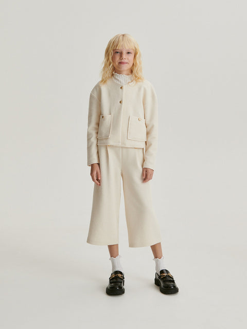 Person wearing a cream-colored outfit with a jacket and pants on a white background