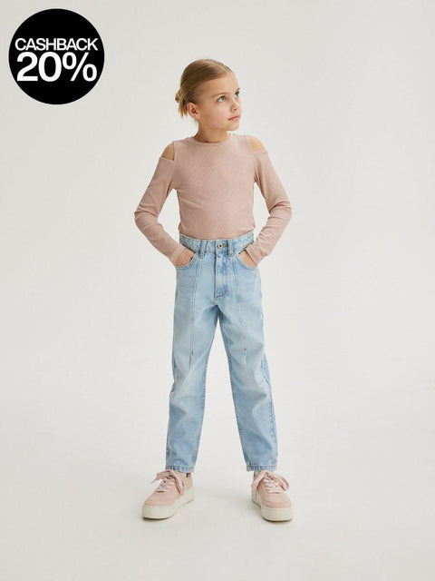 Young girl wearing a pink long-sleeve top and light blue jeans on a white background