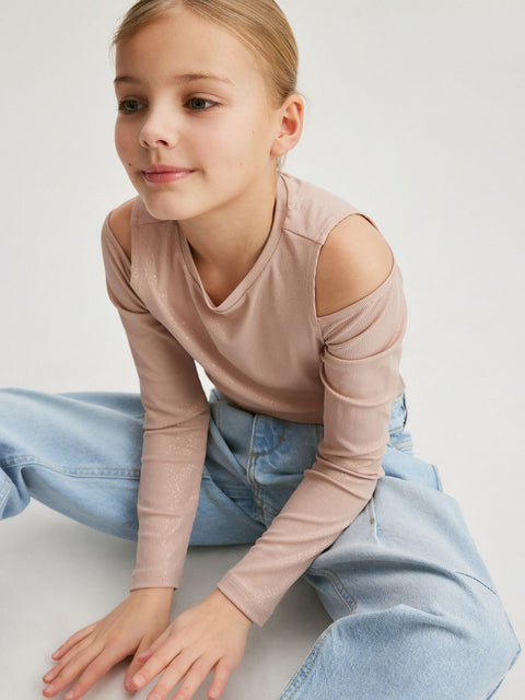 Young girl wearing a beige long-sleeve top and light blue jeans on a white background