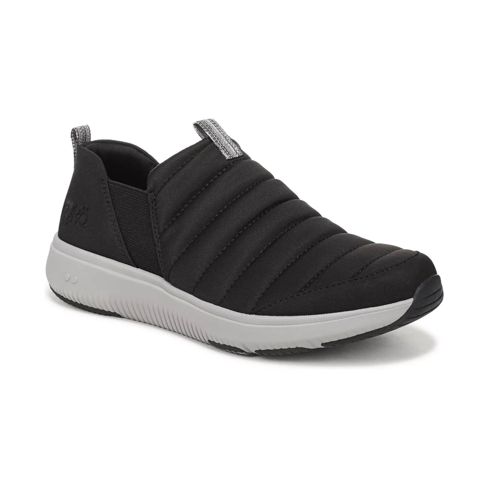 A black slip-on sneaker with a ribbed, quilted upper, a gray pull tab, and a thick white midsole, shown from a three-quarters angle on a white background.