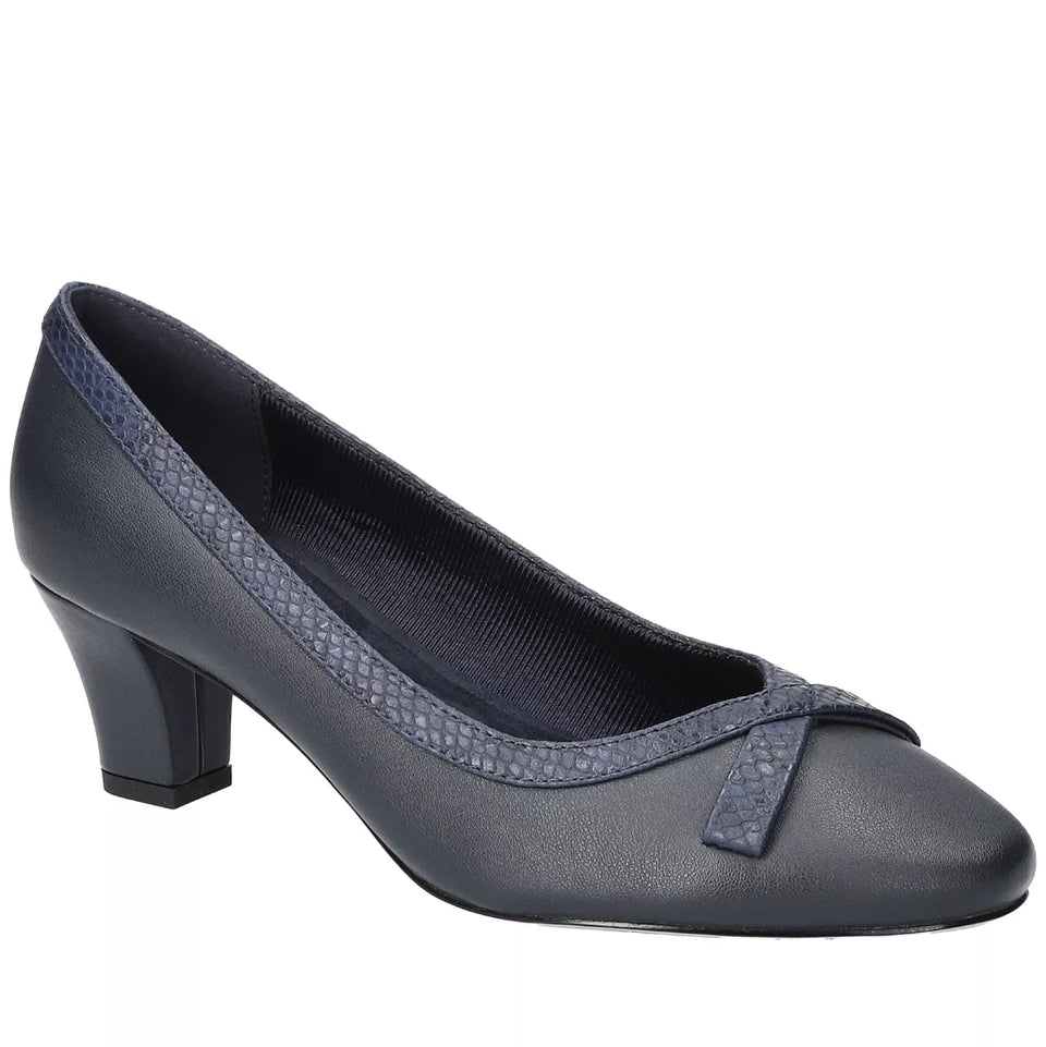 A dark slate blue women's pump shoe with a low block heel, featuring textured patterned trim along the collar and a matching bow detail on the toe, shown against a plain white background.