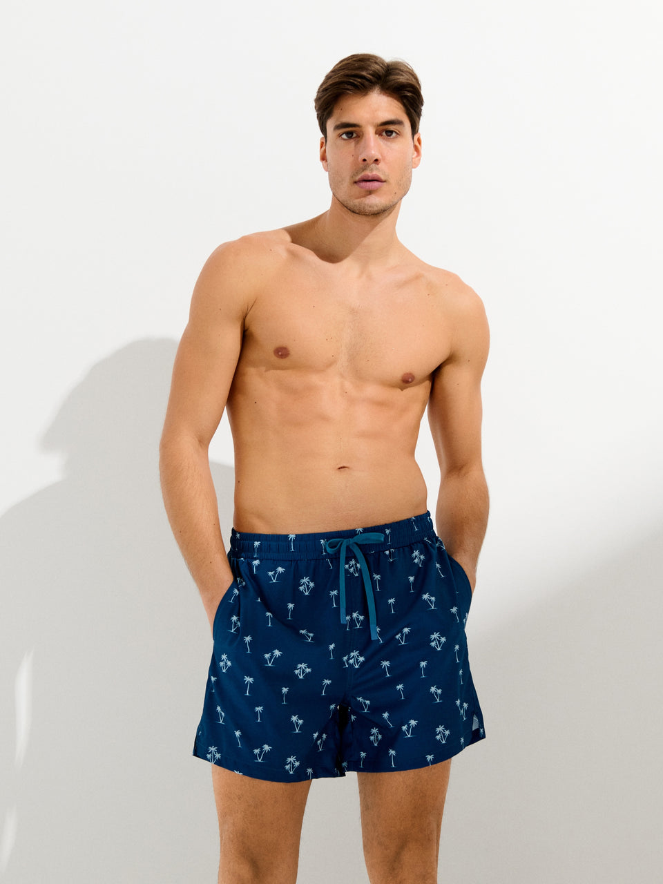 Man wearing navy blue swim shorts with a subtle pattern on a white background