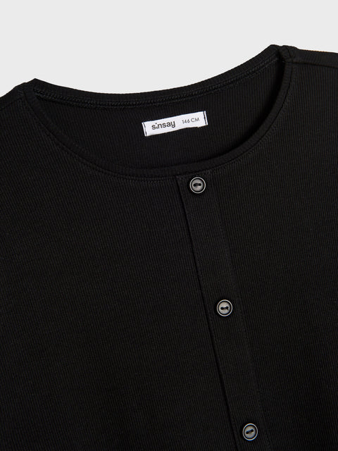 Close-up of a black dress with button details and a visible brand label on a light gray background.