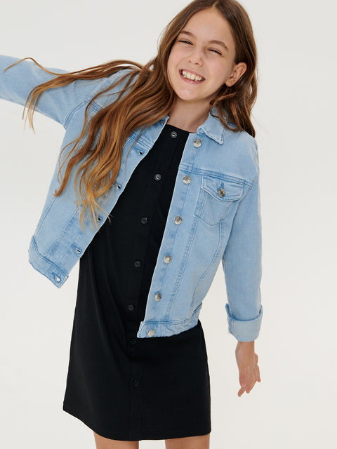 Girl wearing a light blue denim jacket over a black dress on a white background