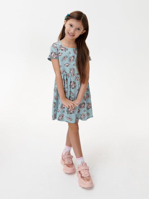 Young girl wearing a light blue floral dress and pink shoes on a white background