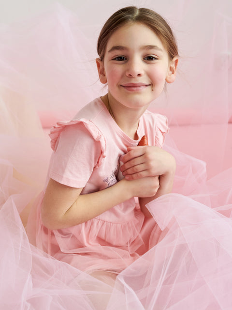 Young girl in a pink dress sitting against a soft pink background