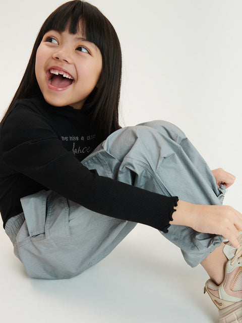 Child sitting on a white floor wearing a black long-sleeve shirt and light gray pants.