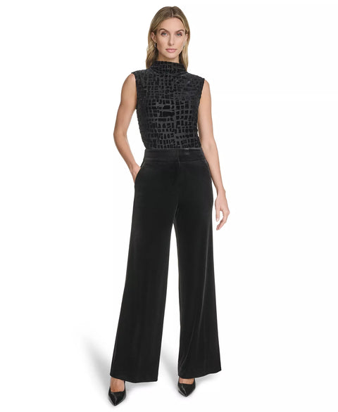 Woman wearing a black sleeveless top with a patterned design and high-waisted black pants on a white background