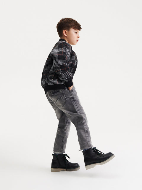 Young boy wearing a plaid shirt, gray jeans, and black boots on a white background