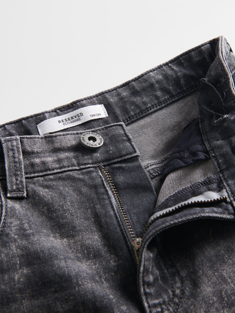 Close-up of a black denim jacket with a brand label on a light gray background