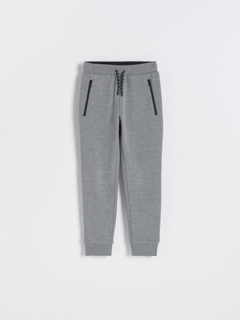 Gray jogger pants with black zippers on a white background