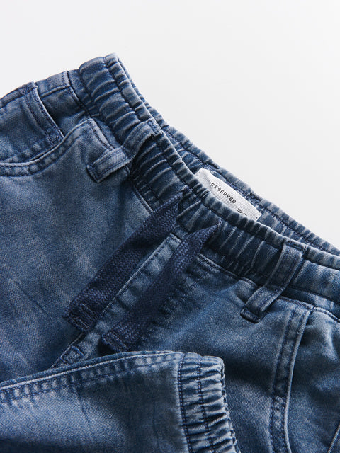 Close-up of blue denim pants with a brand label on a light gray background