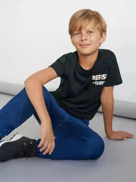 Young boy wearing a black t-shirt with text, sitting on a light gray floor.