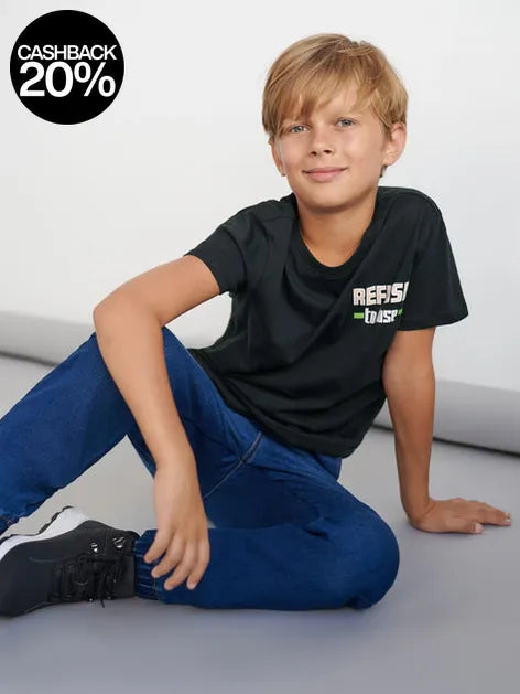 Young boy wearing a black t-shirt with text, sitting on a light gray floor.
