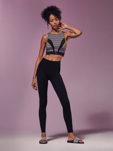 Woman wearing a patterned crop top and black leggings against a purple background