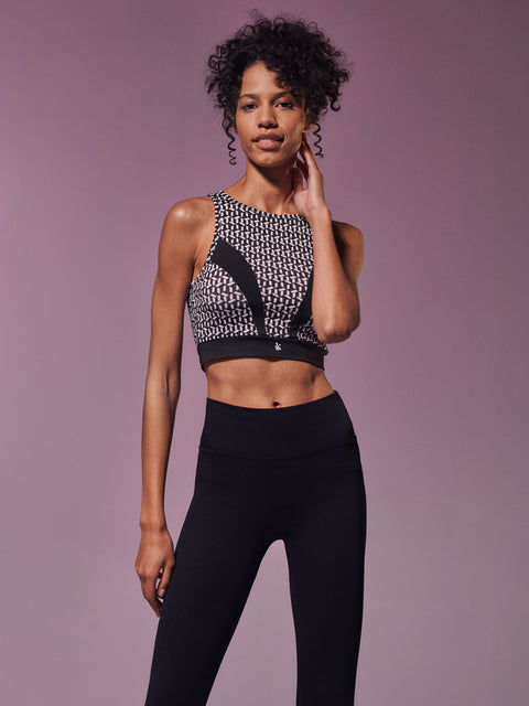 Woman wearing a patterned sports bra and black leggings against a purple background
