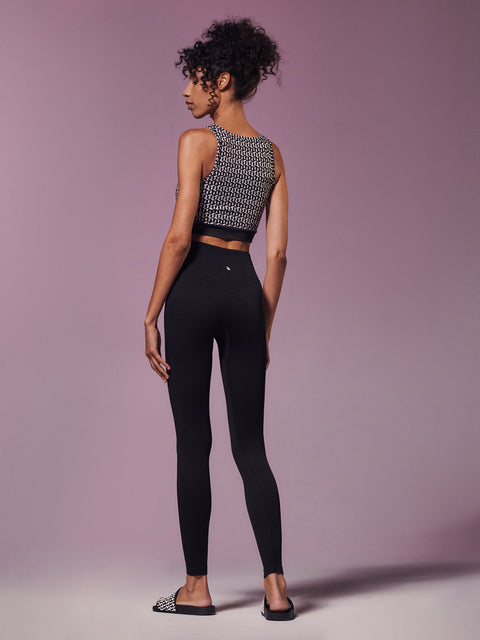 Woman wearing a patterned crop top and black leggings on a plain background