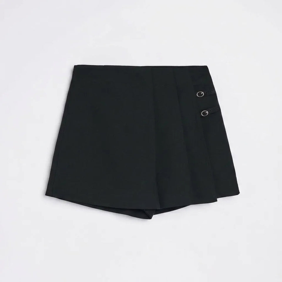 A black wrap-style mini skirt with a pleated front and two silver-tone metal grommets on the side, laid flat against a light gray background.