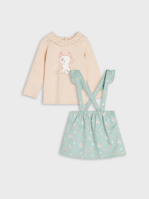 Children's outfit with beige long-sleeve top and green skirt with suspenders on a light gray background