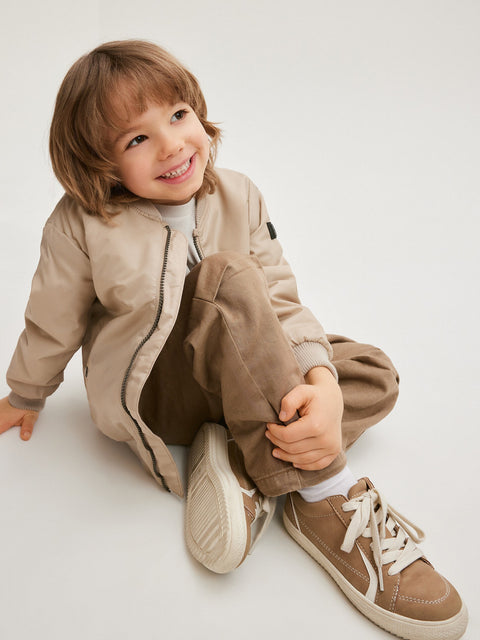 Child wearing a beige outfit with matching shoes on a light background