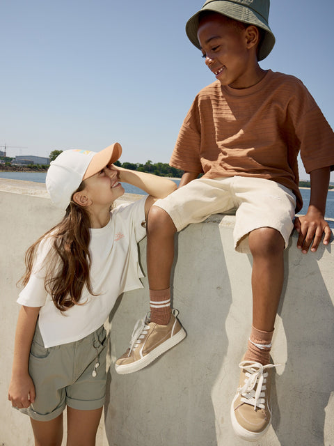Two children sitting on a concrete ledge by a body of water, wearing casual clothing.