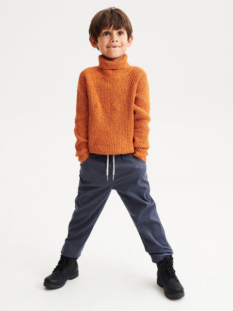 Child wearing an orange sweater and blue pants on a white background
