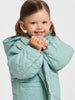 Young girl wearing a light blue quilted coat on a plain background