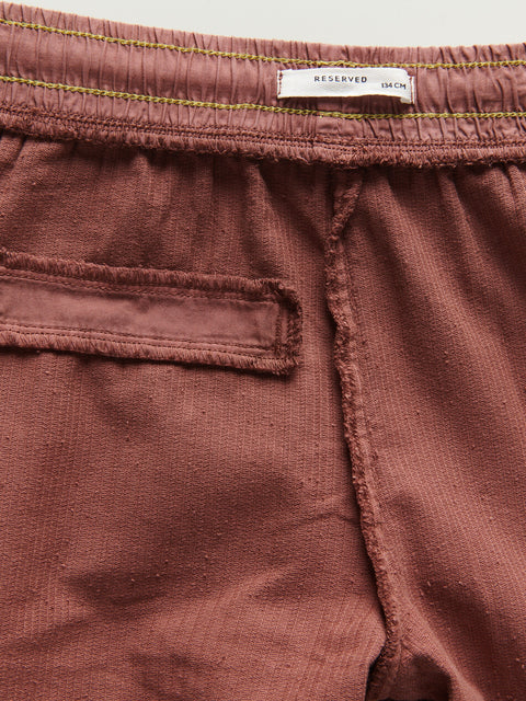 Close-up of maroon shorts with a 'RESERVED' tag on a light gray background