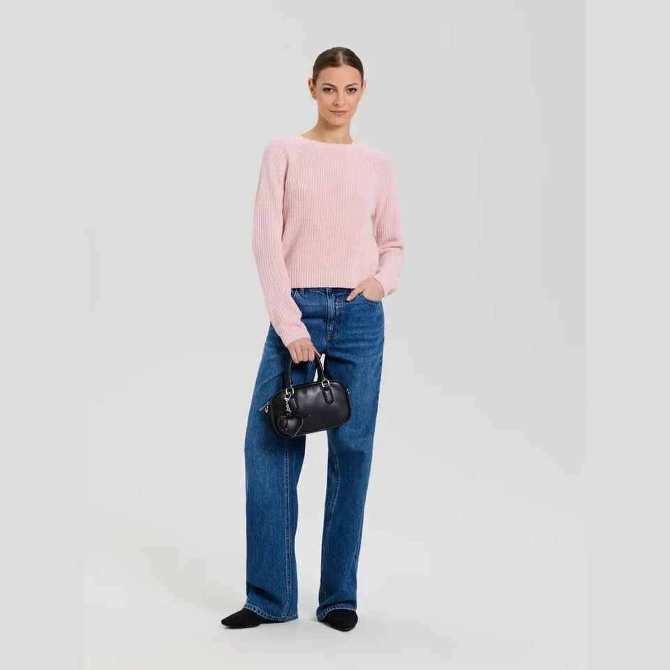 A woman modeling a light pink ribbed knit sweater, blue wide-leg jeans, and a small black handbag against a light gray studio background.