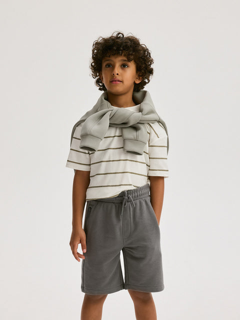 Child wearing a striped shirt and gray shorts on a white background