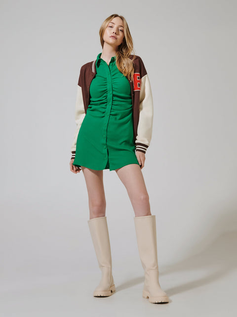 Woman wearing a green dress with a brown and red jacket and beige knee-high boots on a white background