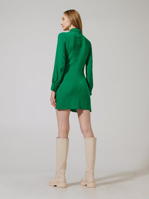 Woman wearing a green dress and beige knee-high boots on a plain background