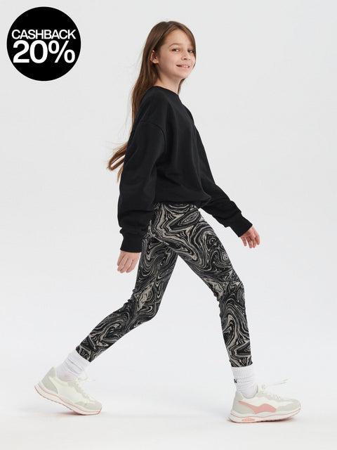 Girl wearing a black sweatshirt and patterned leggings on a white background