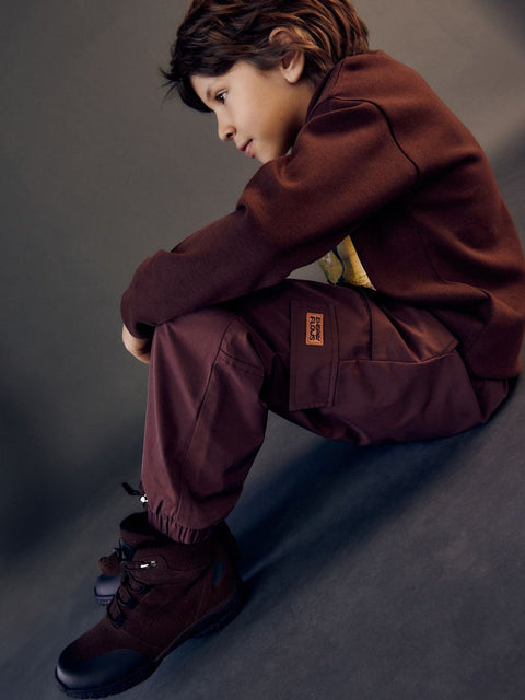 Person wearing a brown outfit sitting on a gray surface