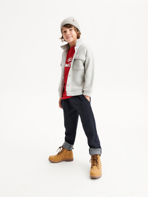 Child wearing a gray jacket, red shirt, black pants, and brown boots on a white background