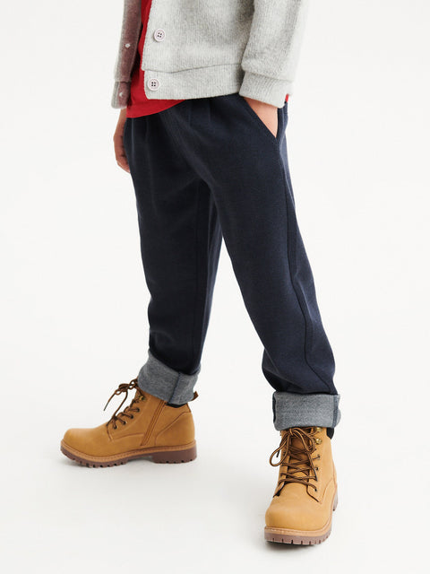 Person wearing navy pants, a gray sweater, and brown boots on a white background