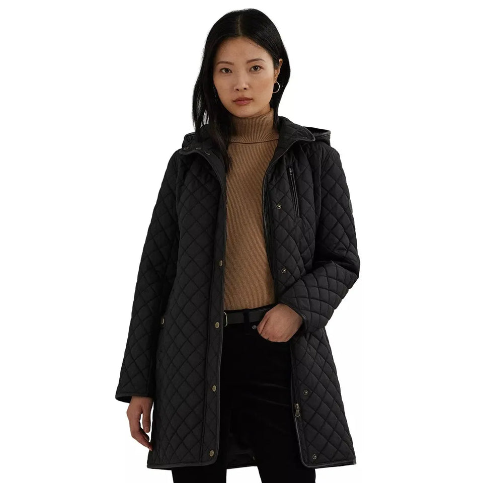 A woman modeling a black diamond-quilted hooded coat over a brown turtleneck sweater and black pants, set against a plain white background.