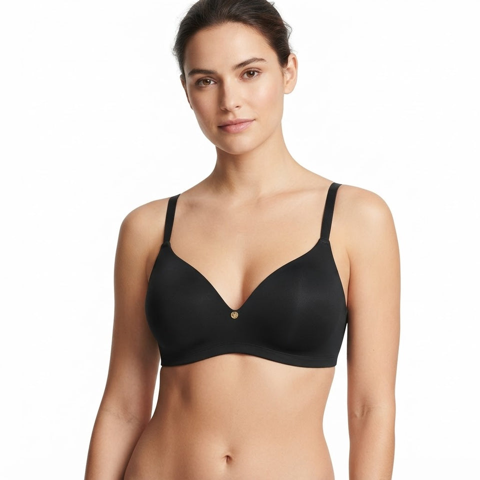 A woman modeling a black wireless bra with thin shoulder straps and a small gold button at the center, photographed against a plain white studio background.