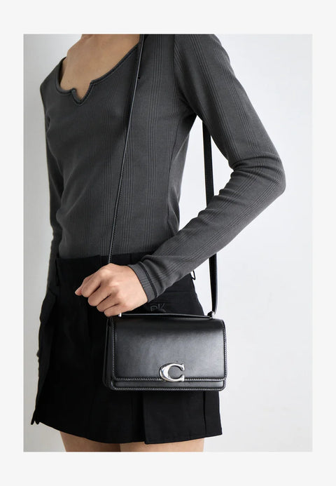 Person wearing a black outfit with a black handbag featuring a silver clasp on a light gray background