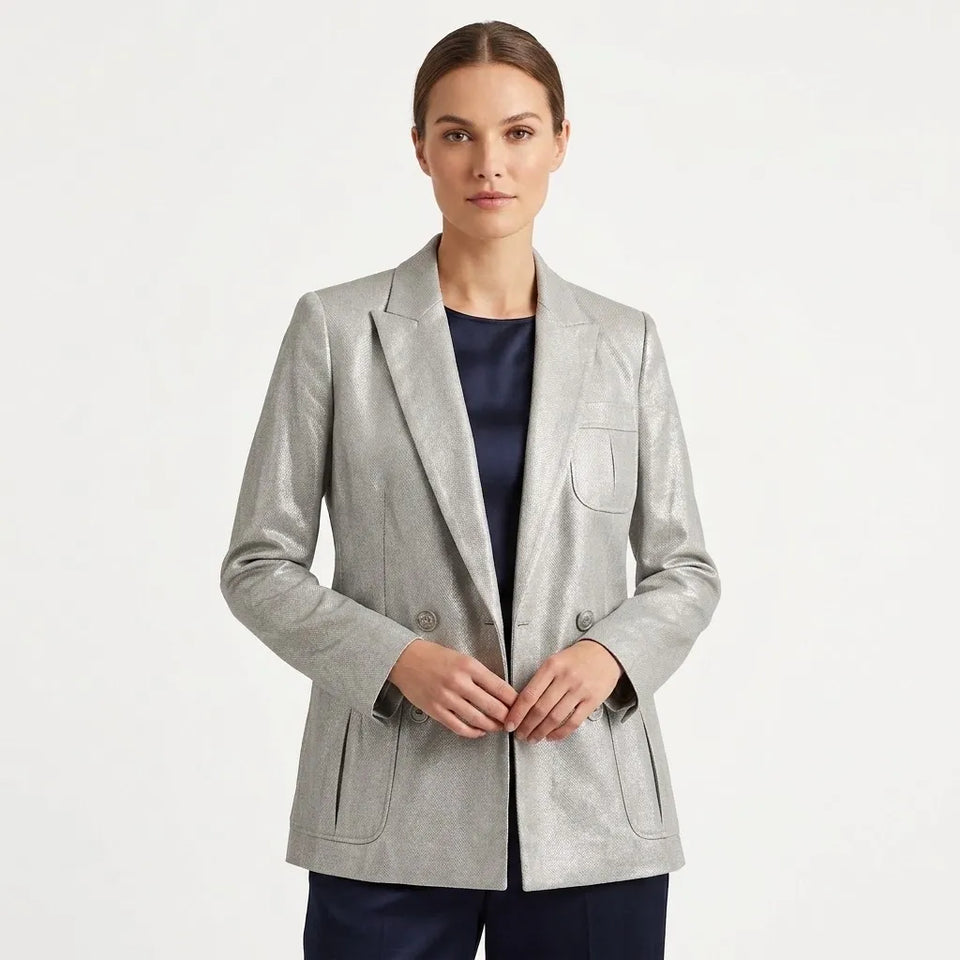 A woman modeling a light gray textured double-breasted blazer over a navy blue top and navy trousers, photographed against a clean white studio background.
