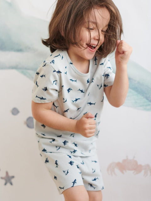 Child wearing a white shirt with blue patterns, sitting on a bed.
