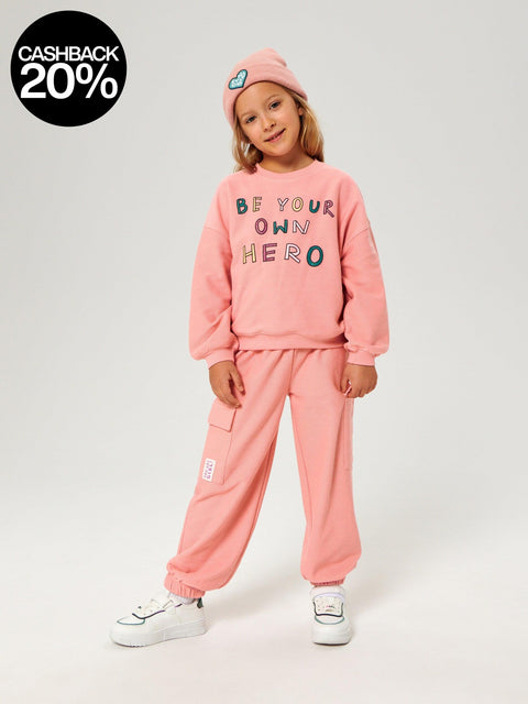 Child wearing a pink outfit with 'Be your own hero' text on a white background