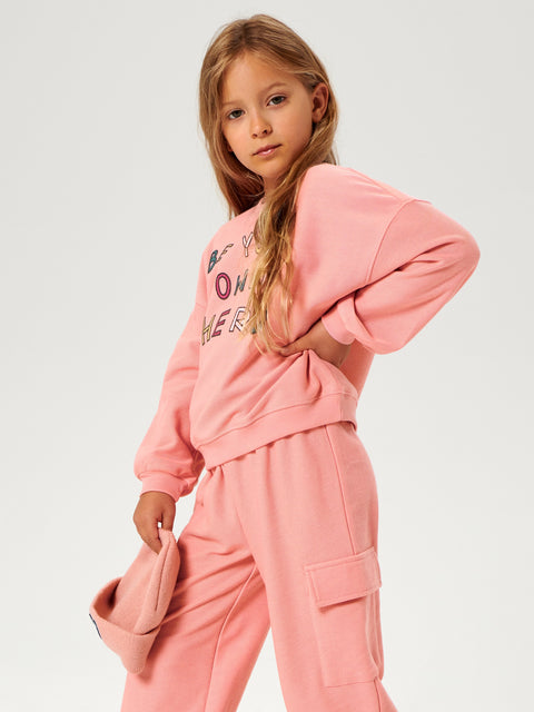 Young girl wearing a pink sweatshirt and pants set on a white background