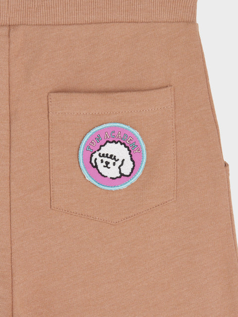 Brown sweatpants with a patch on the pocket featuring a dog illustration and text.