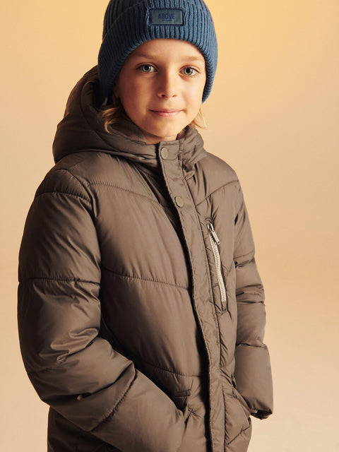 Child wearing a brown puffer jacket and blue beanie on a beige background