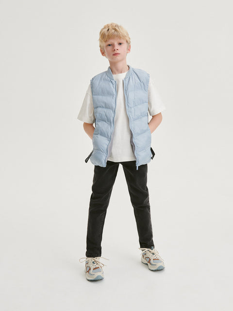 Child wearing a light blue puffer vest over a white shirt on a white background