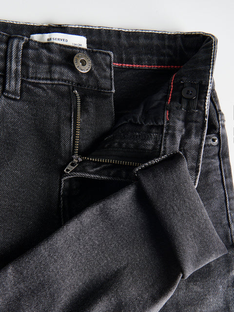 Close-up of black denim jeans with a visible brand label on a white background