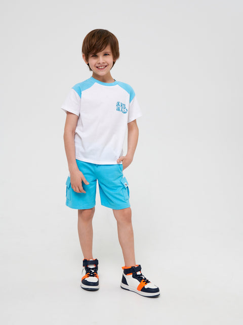 Child wearing a white and blue shirt with turquoise shorts on a light gray background