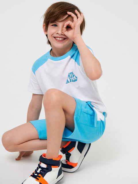 Child wearing a white and blue outfit with a logo, posing on a light gray background