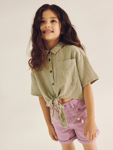 Young girl wearing a green shirt and pink shorts on a plain background
